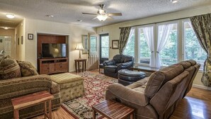 A living room with a sofa, ottoman, and armchair, a television, and a ceiling fan. - 05234 - 34 South Pego Way (Hot Springs)