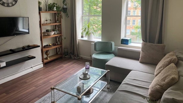 Un salon moderne avec un téléviseur à écran plat, une table basse en verre, un canapé, un fauteuil et une bibliothèque.