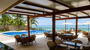 An outdoor pool area with tables and chairs, a clear view of the ocean, and a covered seating area. - Casa BeiraMar 4QTS Piscina-SH031 (Ipojuca)