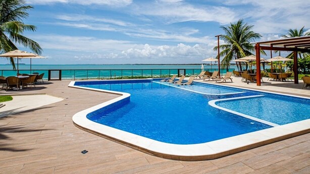 A pool area with two pools, lounge chairs, and umbrellas. - Casa BeiraMar 4QTS Piscina-SH031 (Ipojuca)