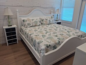 A neatly arranged bedroom with a white bed, matching nightstands, and a wooden floor.