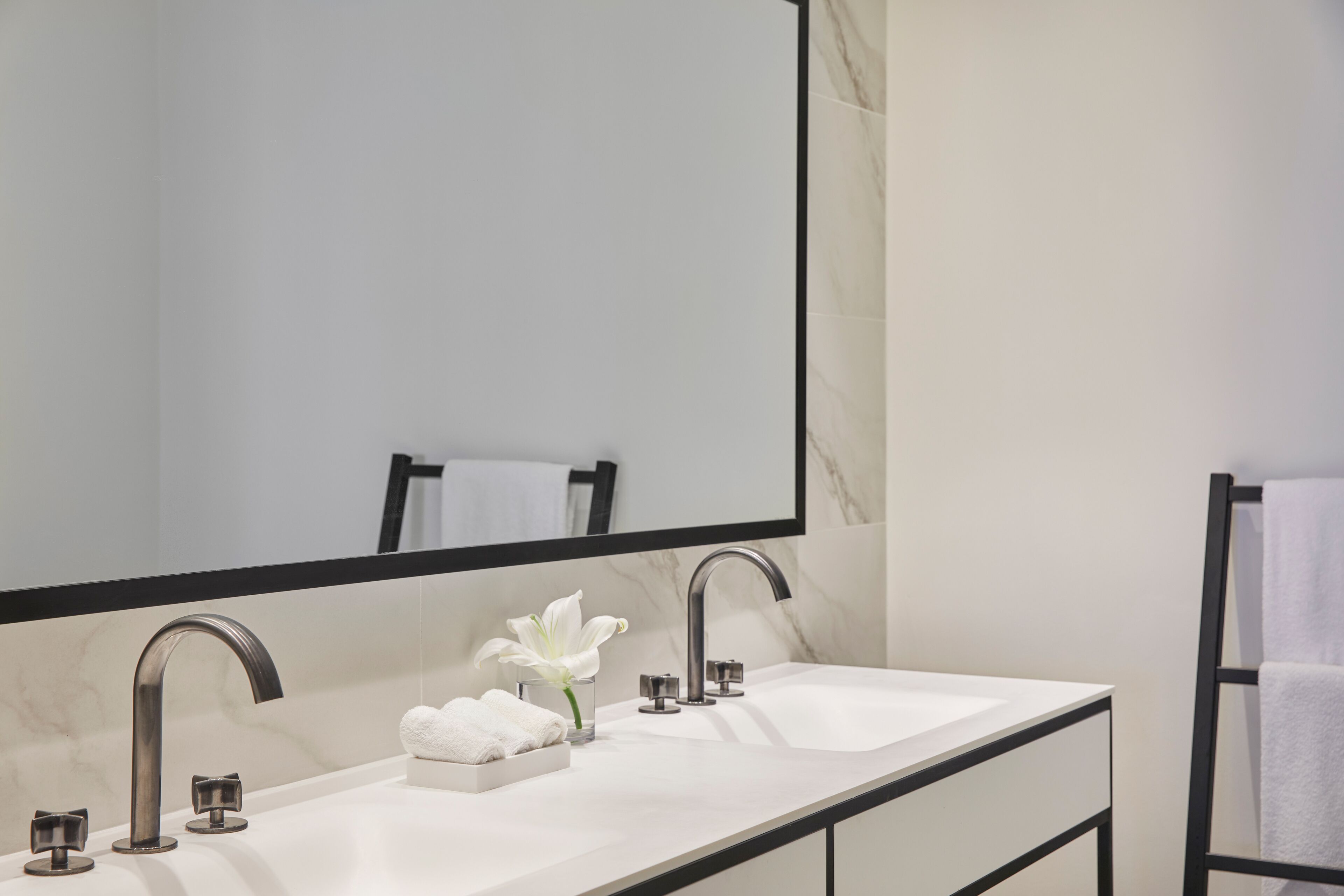 A modern bathroom with a double sink, a large mirror, and a vase with a white flower.