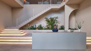 A modern reception area with a staircase, a reception desk, and indoor plants.