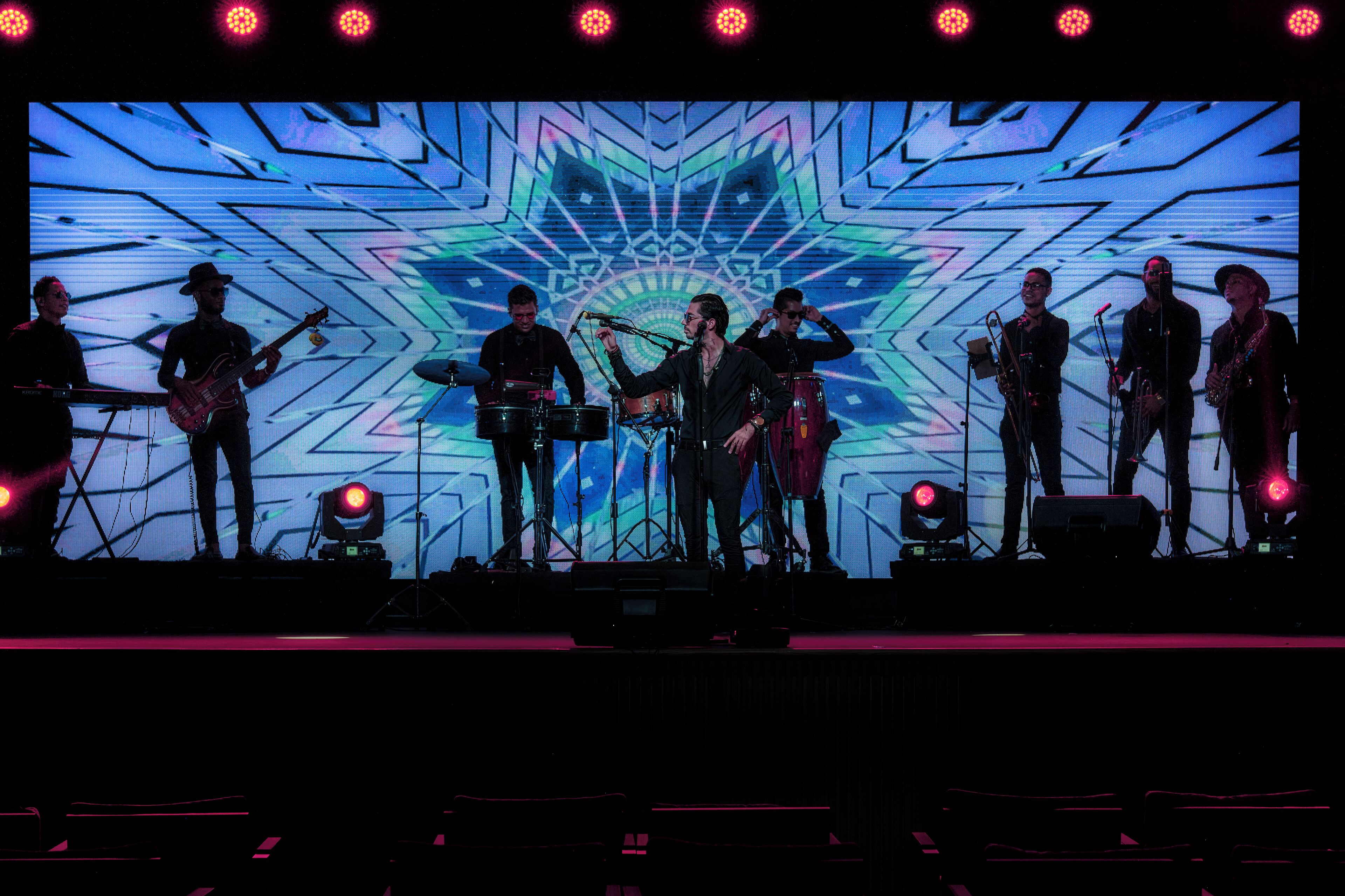 Un groupe de musique se produit sur une scène, avec un grand écran LED en arrière-plan qui affiche un motif géométrique.