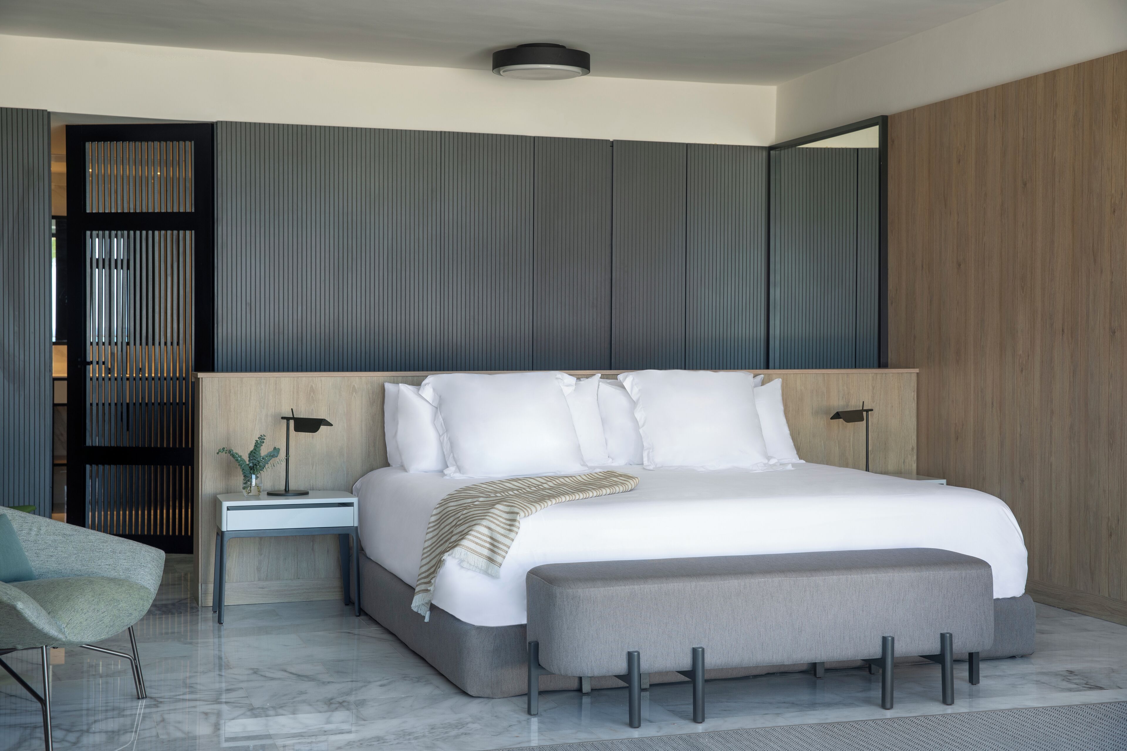 Une chambre à coucher moderne avec un grand lit, des tables de chevet, un banc et un miroir.