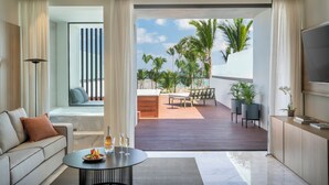 A modern living room with a sofa, a coffee table with drinks, and a view of a deck with outdoor furniture and palm trees. - The Excellence Club at Finest Punta Cana Adults Only - All Inclusive (Punta Cana)