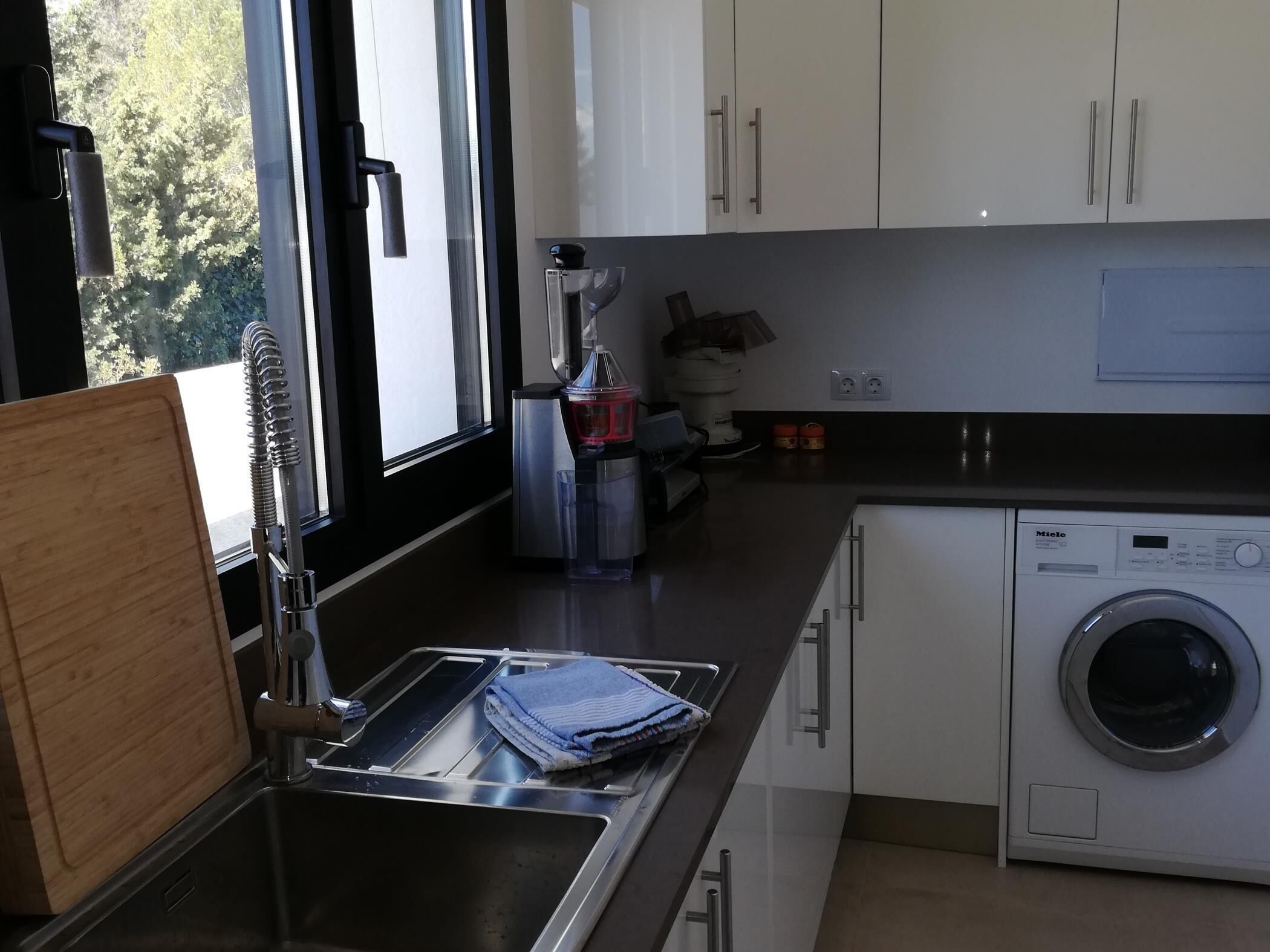 Una cucina moderna con lavatrice integrata, elettrodomestici in acciaio inossidabile e abbondante luce naturale proveniente da ampie finestre.