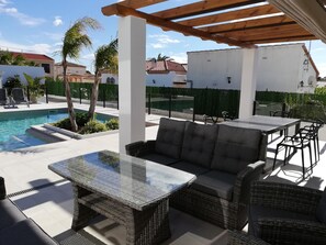 Uma área externa coberta com piscina, mobiliário de vime e um pérgola.