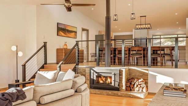 Una sala de estar moderna con chimenea, un sofá, una zona de comedor con sillas y una escalera.