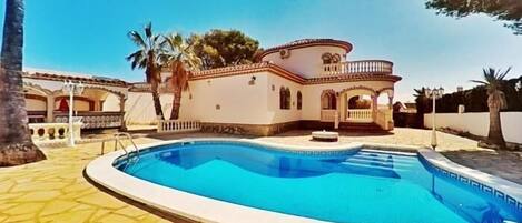 Relax by the pool surrounded by a Mediterranean-style home with a balcony and arches.