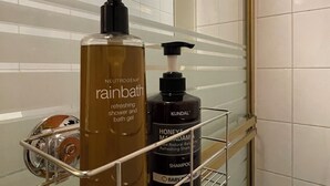 Un baño con espejo, un estante metálico que contiene una botella de gel de ducha Neutrogena Rainbath y una botella de champú KUNDAL Honey & Mandala.
