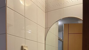 Un baño con paredes de azulejos blancos, un lavabo blanco, un espejo y un dispensador de jabón.