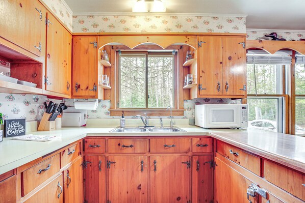 A kitchen with wooden cabinets, a sink, a microwave, and a window with a view of trees. - Private Dock, Deck & Yard: Deerskin Lake Retreat! (Eagle River)