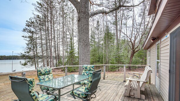 A deck with a glass table and chairs, overlooking a body of water and surrounded by trees. - Private Dock, Deck & Yard: Deerskin Lake Retreat! (Eagle River)