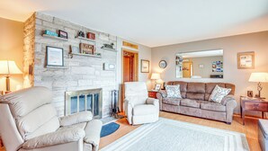 A living room with a stone fireplace, a sofa, a recliner, and a coffee table. - Private Dock, Deck & Yard: Deerskin Lake Retreat! (Eagle River)