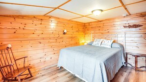 A wooden cabin room with a bed, a rocking chair, and a small table. - Private Dock, Deck & Yard: Deerskin Lake Retreat! (Eagle River)