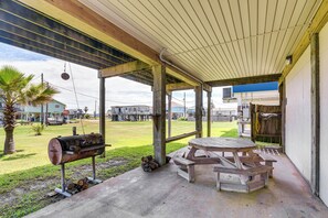 Eine überdachte Terrasse im Freien mit Grill, Picknicktisch und Bänken.