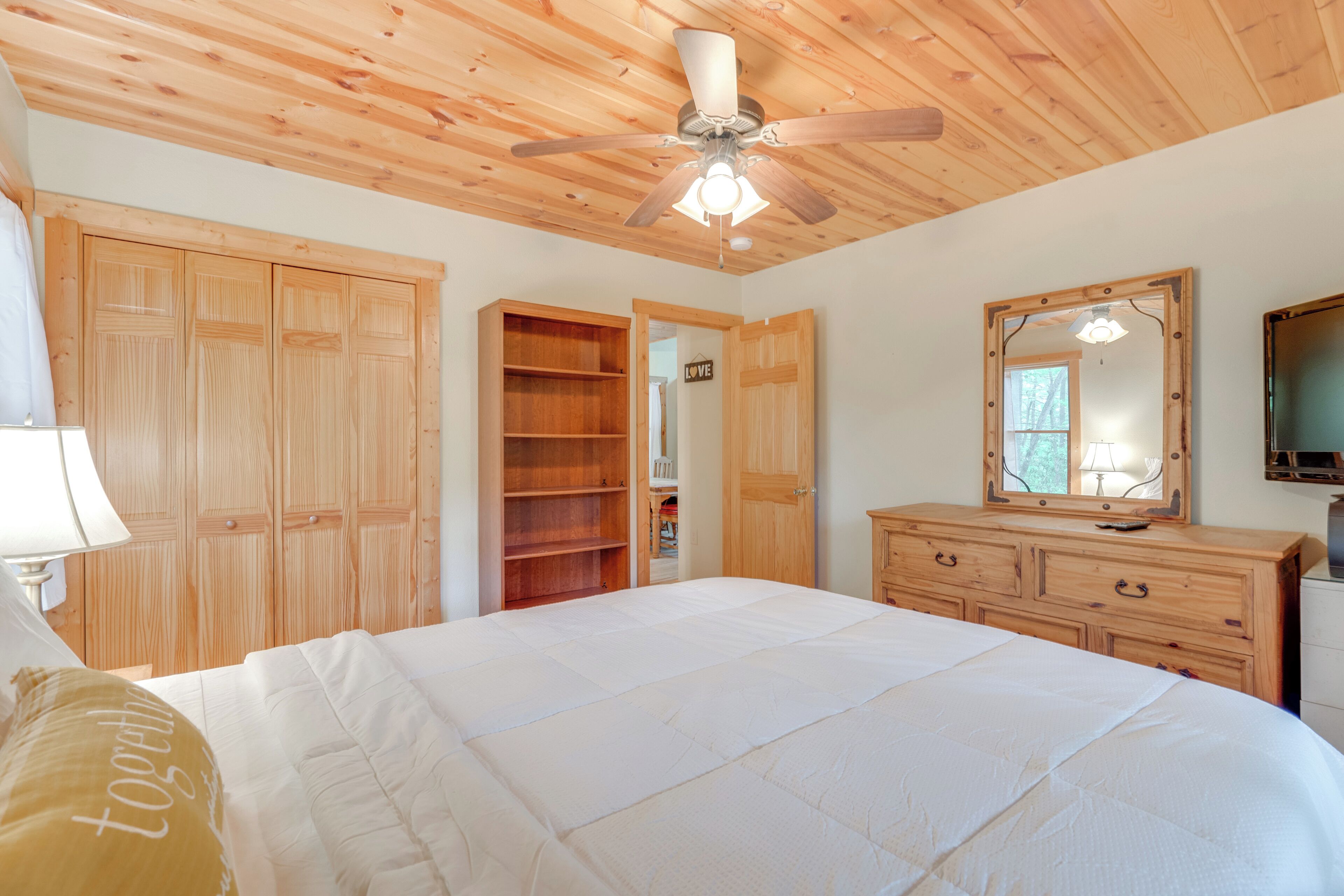 Une chambre avec un grand lit, une armoire en bois et un ventilateur de plafond.