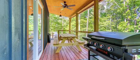 A covered outdoor deck with a grill, picnic table, and ceiling fan.
