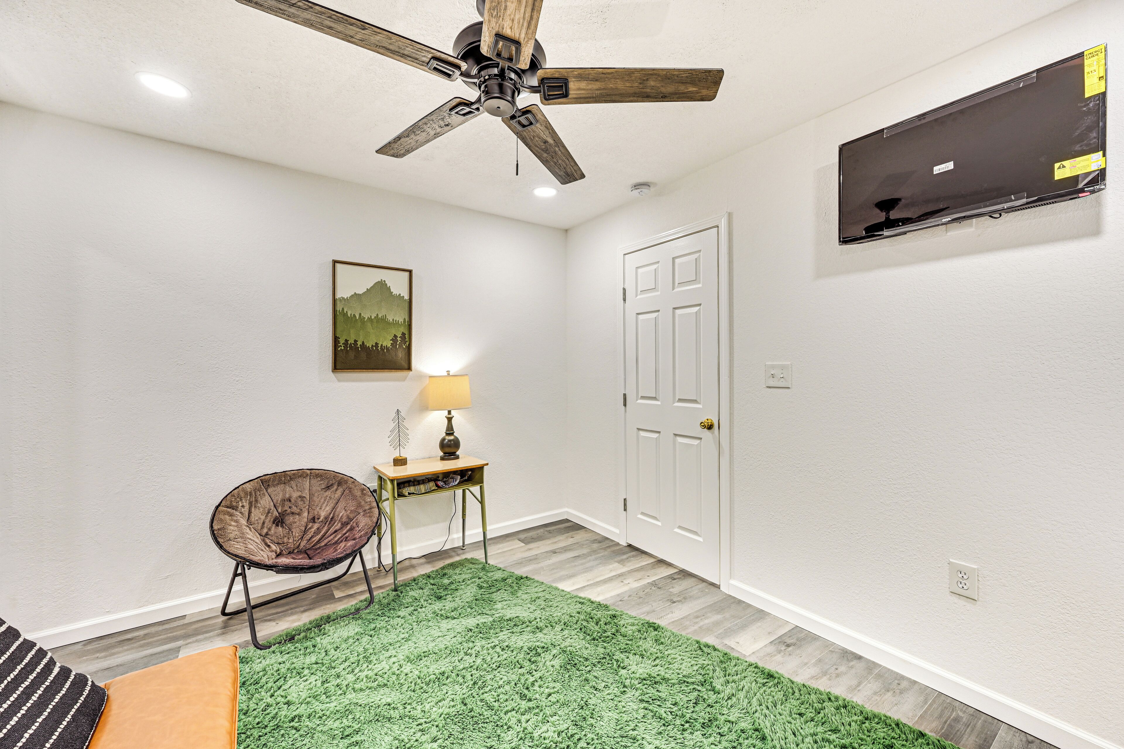 Una habitación con ventilador de techo, alfombra verde, una silla, una lámpara y una puerta.