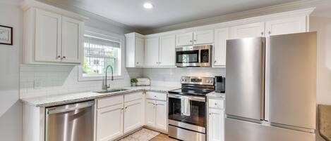 A modern kitchen with white cabinetry, stainless steel appliances, and a wooden floor.