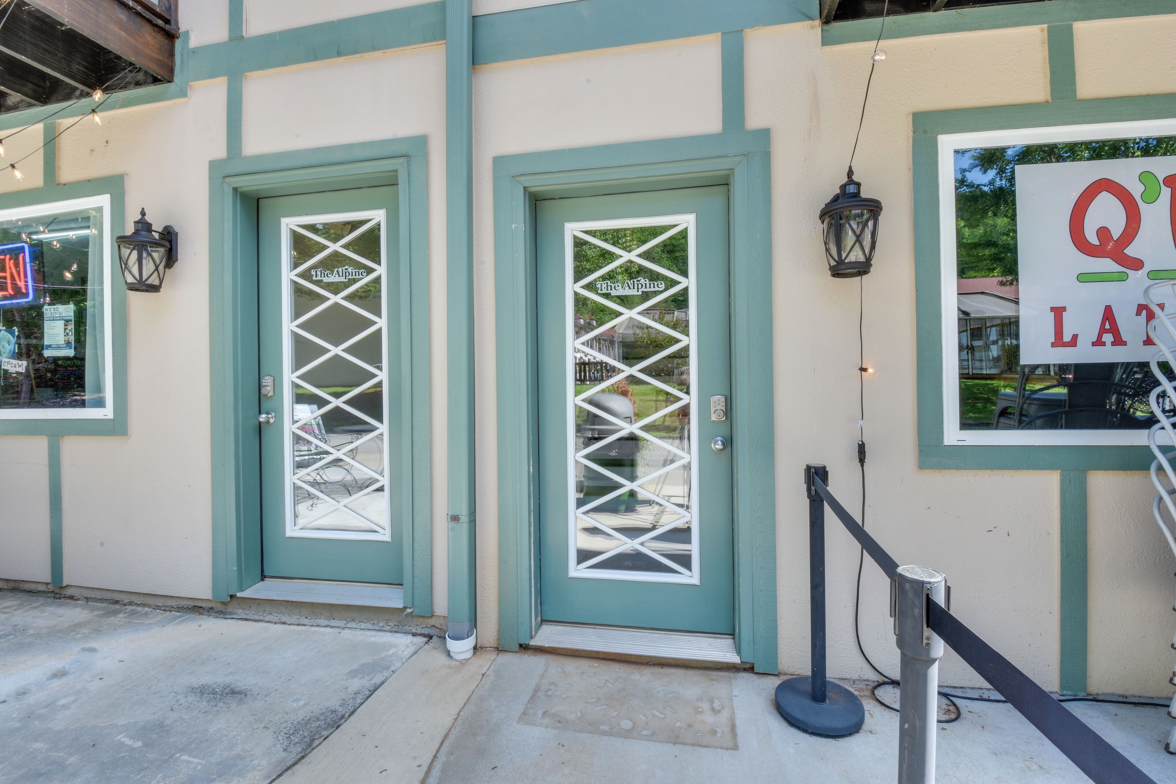 A building with teal-colored doors and windows, a sign reading "The Alpine," and a queue barrier outside.