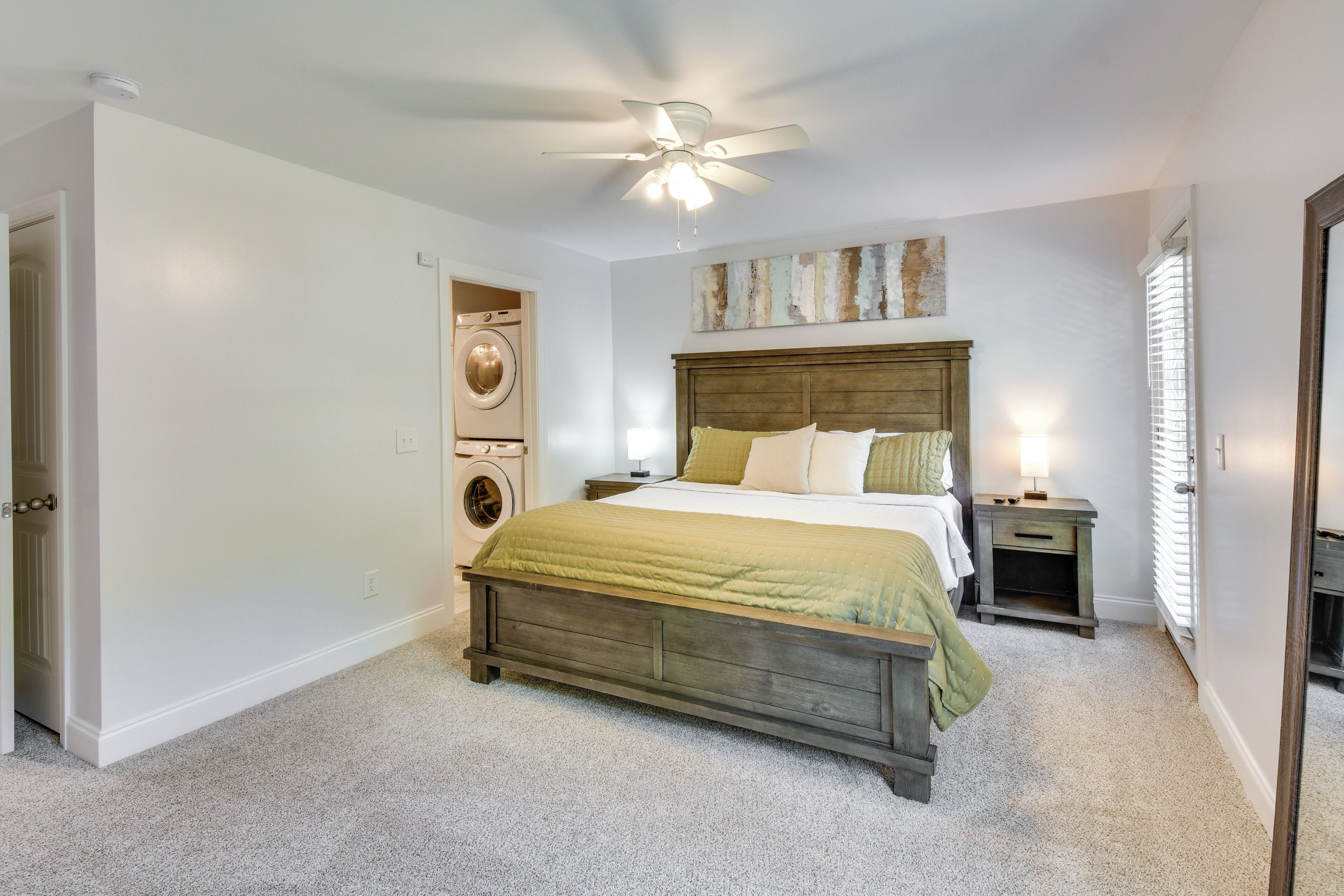 A bedroom with a wooden bed, a ceiling fan, a washing machine, and a nightstand with a lamp.