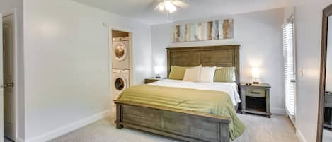 A bedroom with a wooden bed, a ceiling fan, a washing machine, and a nightstand with a lamp.