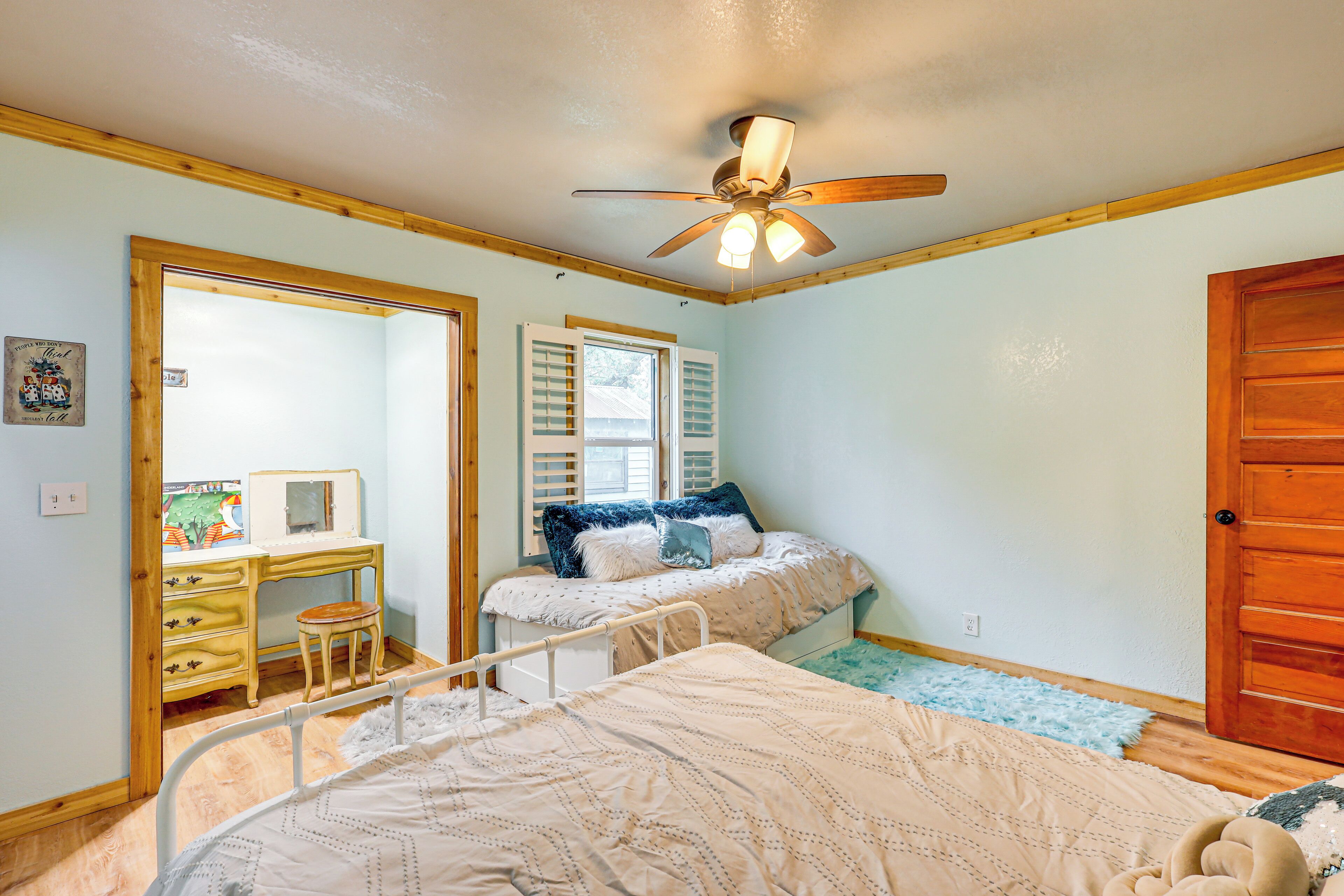 A bedroom with a bed, a desk, and a chair. There is a door and a window with shutters.
