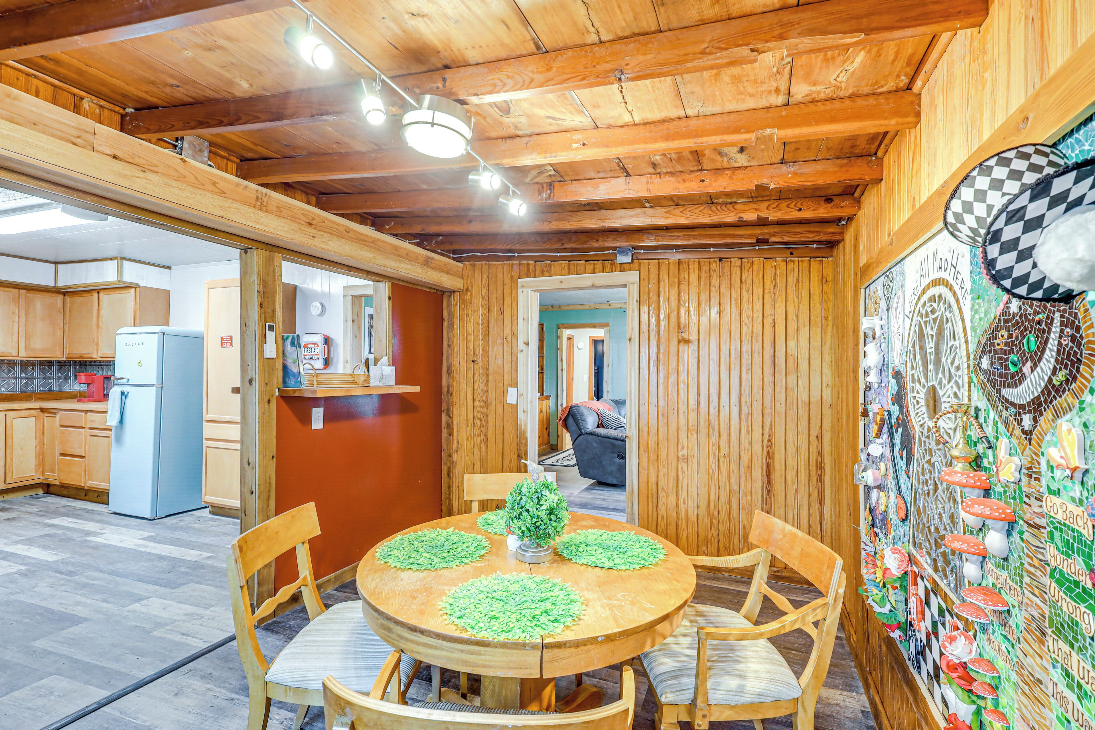 A wooden interior with a dining area featuring a round table and chairs, a kitchen with wooden cabinets, and a wall with a colorful mural.