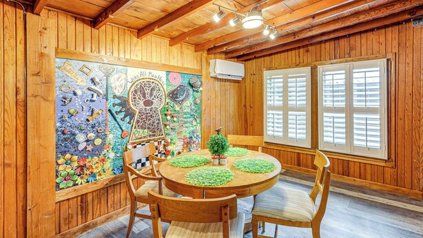 A wooden interior with a round wooden table, four chairs, a decorative wall with a mosaic, and a window with shutters. - Deck, Hot Tub & Lake View: Brownwood Home! (Brownwood)