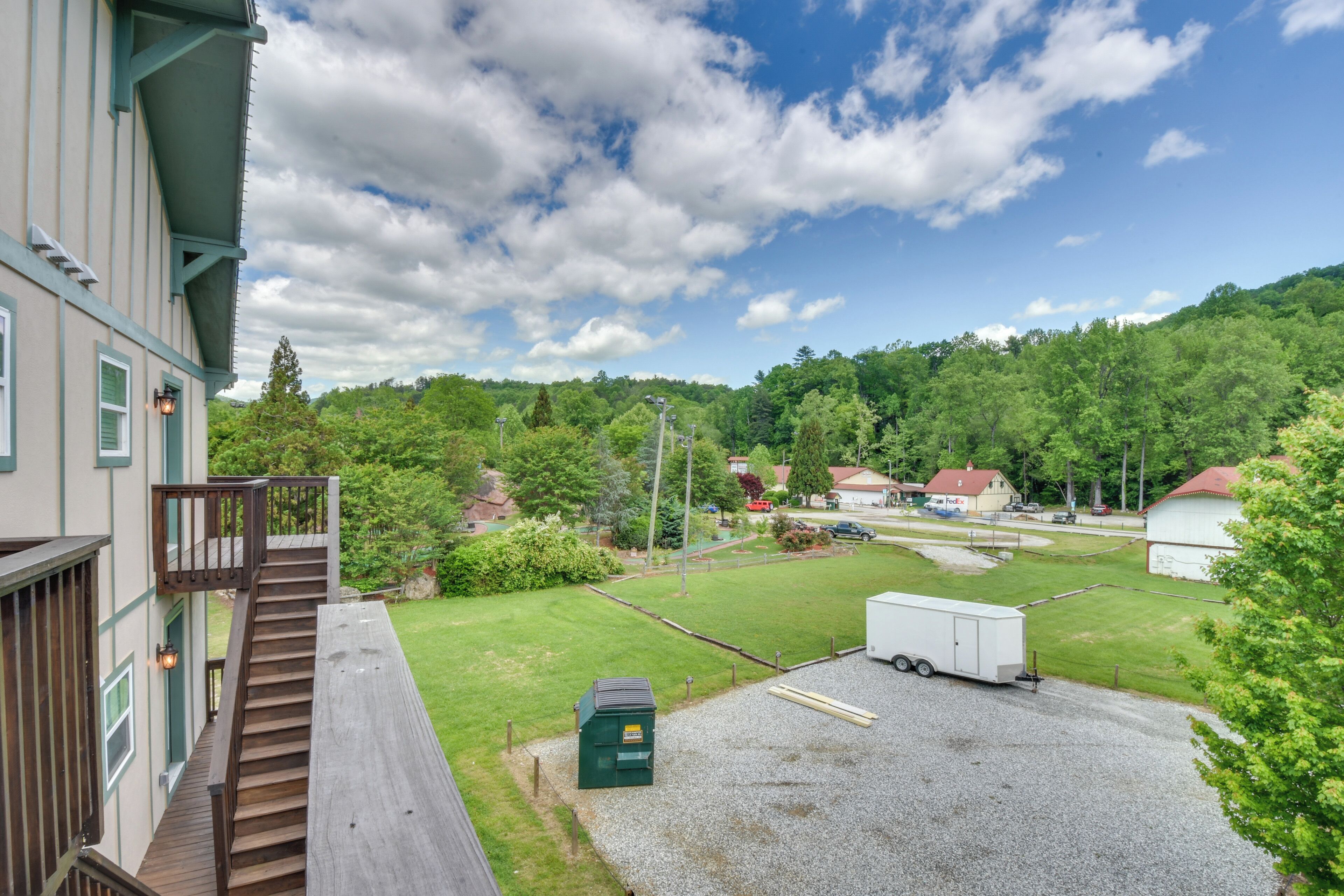 A residential area with a house, a wooden deck, a gravel driveway, and a green dumpster.