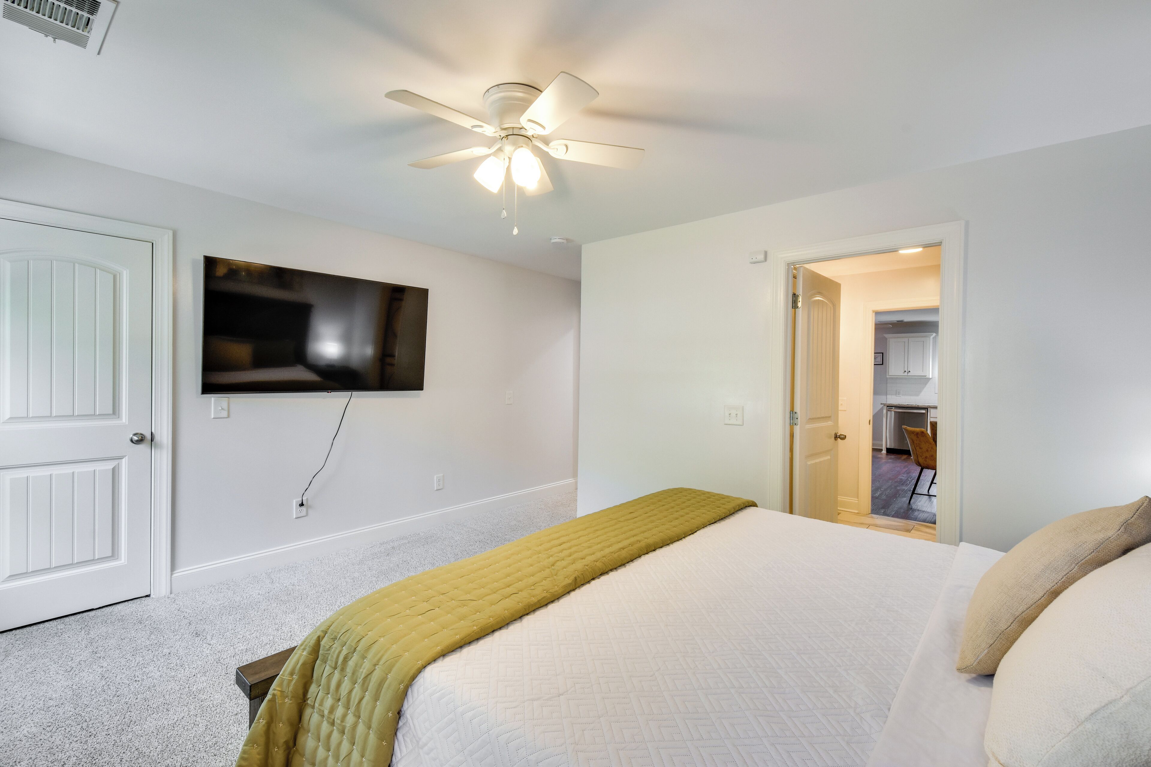 A bedroom with a bed, a ceiling fan, a TV mounted on the wall, and a door leading to a bathroom.