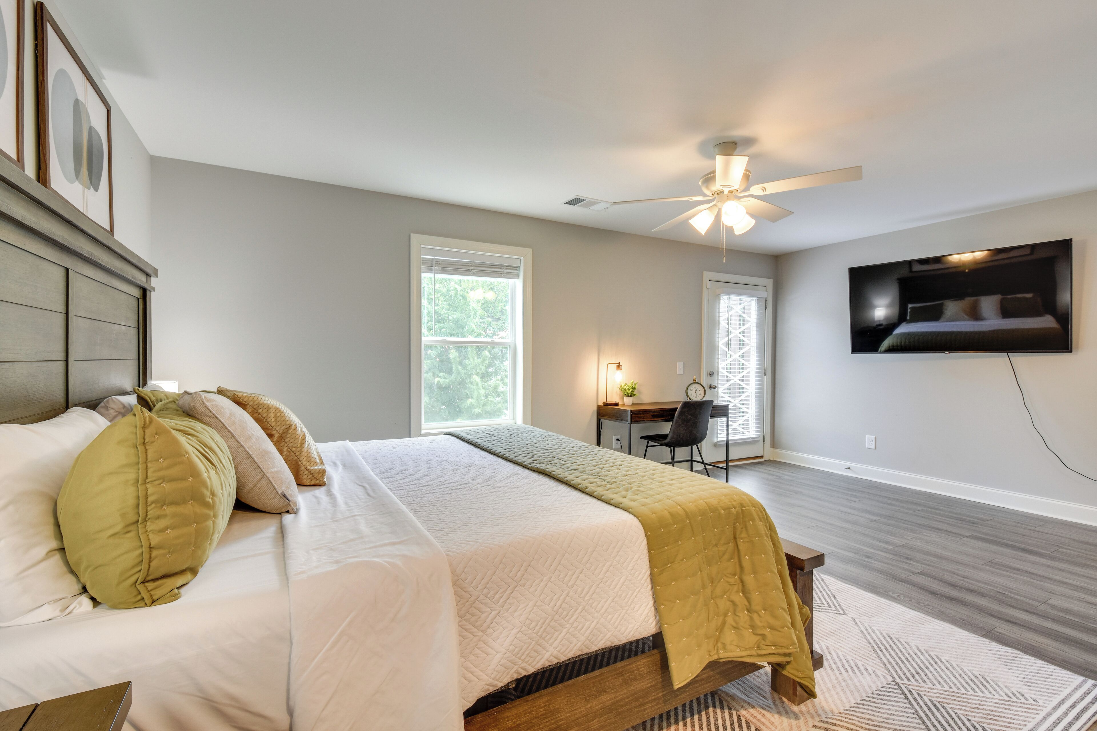 A bedroom with a bed, a desk, a chair, a TV, and a ceiling fan.