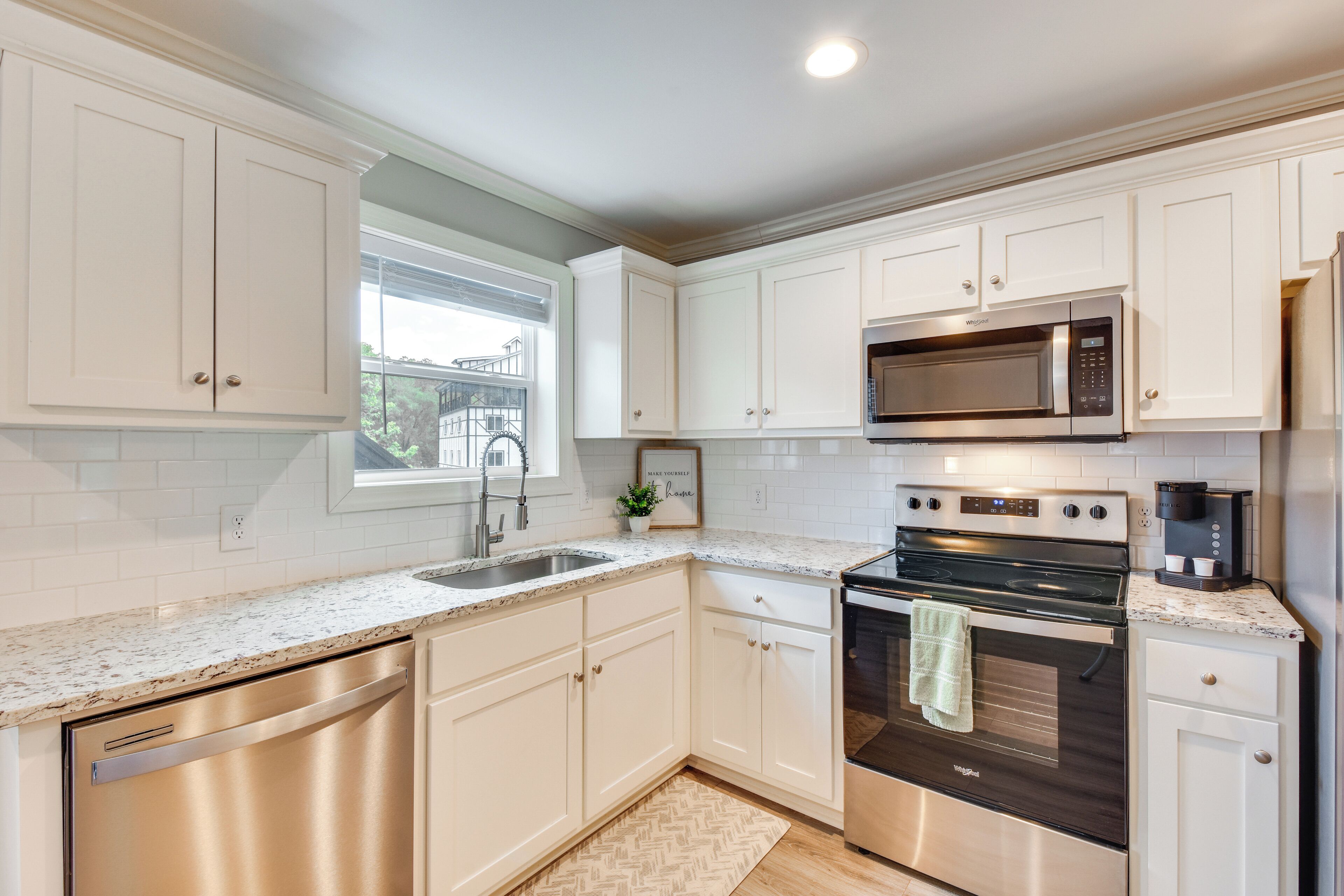 A modern kitchen with white cabinetry, stainless steel appliances, and a window providing natural light.