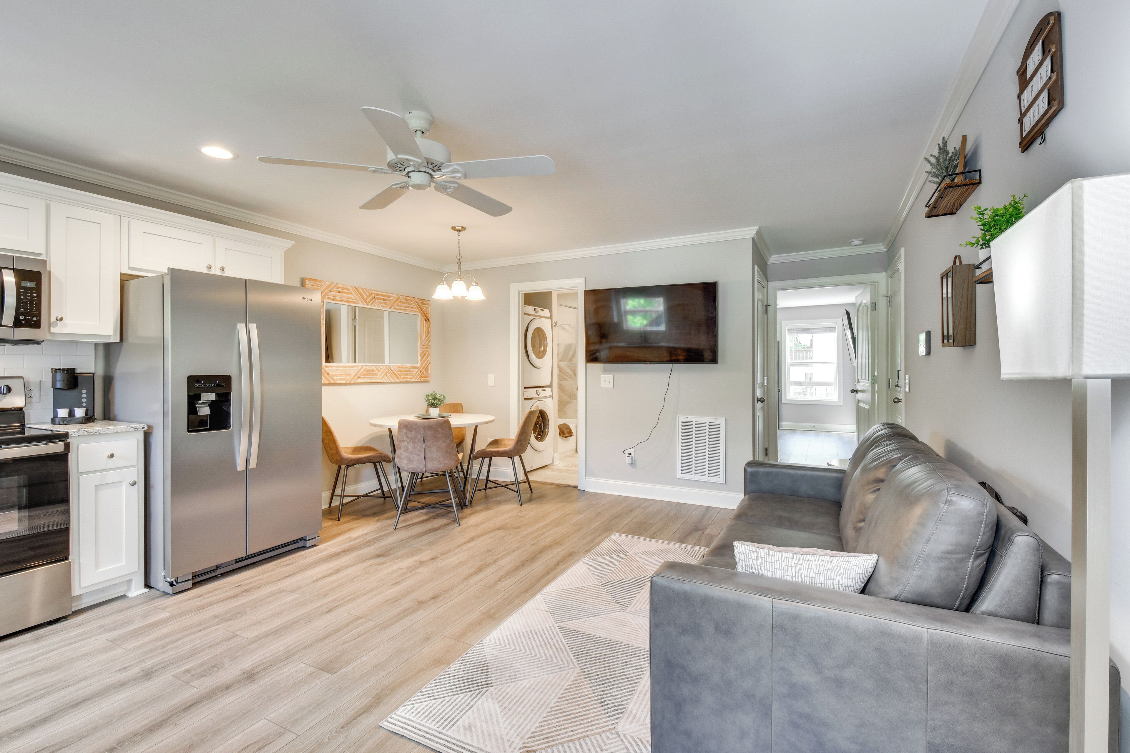 A modern kitchen with a refrigerator, microwave, and oven. There is a dining area with a table and chairs. A gray couch is in the living area.