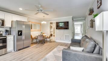 A modern kitchen with a refrigerator, microwave, and oven. There is a dining area with a table and chairs. A gray couch is in the living area.