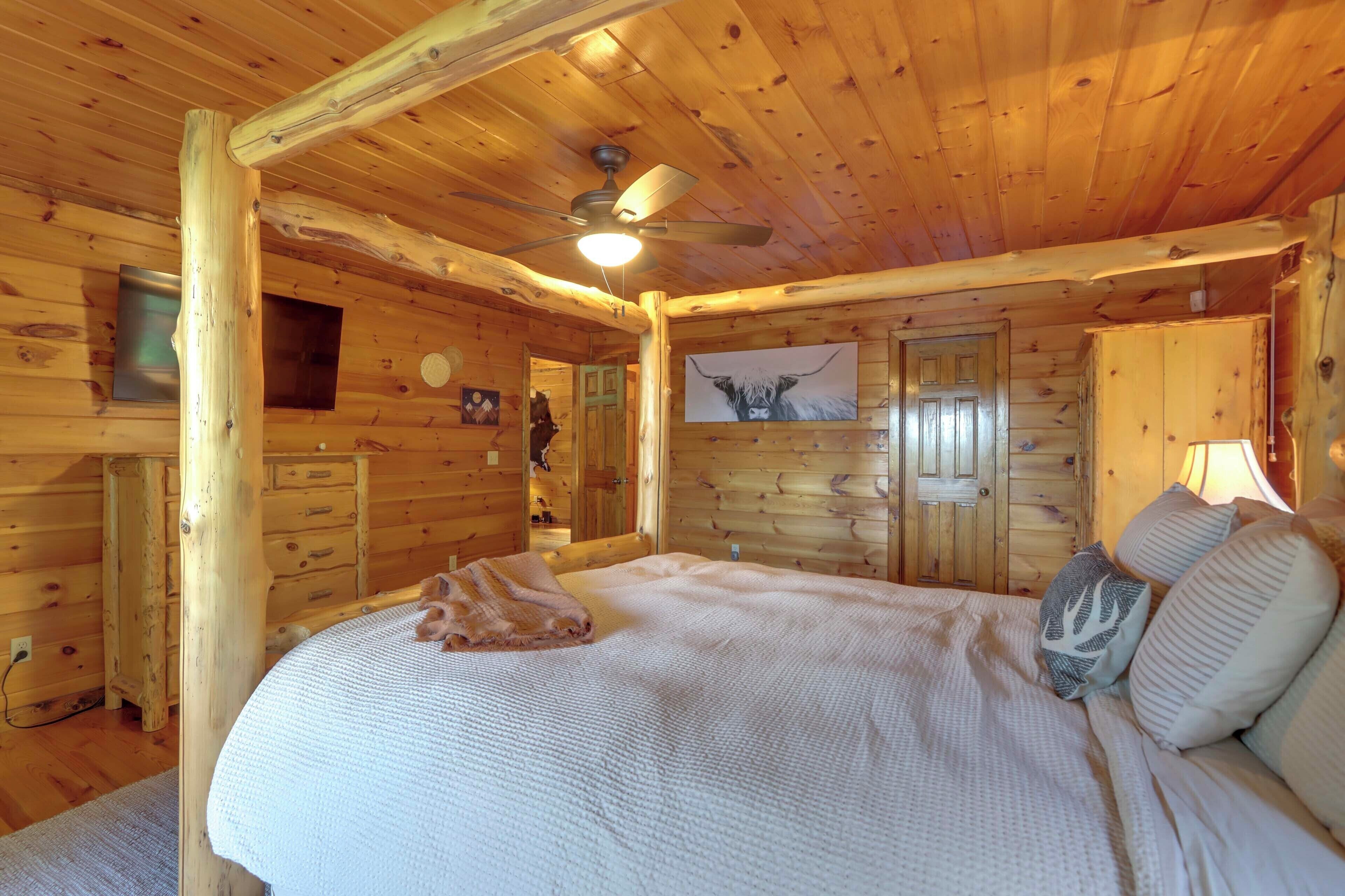 Ein gemütliches Schlafzimmer in einer Blockhütte mit einem Bett, Kissen, einem Deckenventilator, Holzwänden und einem gerahmten Bild an der Wand.