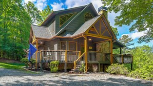 A large, two-story house with a wrap-around porch, a stone chimney, and a flag. - Family Friendly: Hot Tub Haven in Mineral Bluff! (Mineral Bluff)
