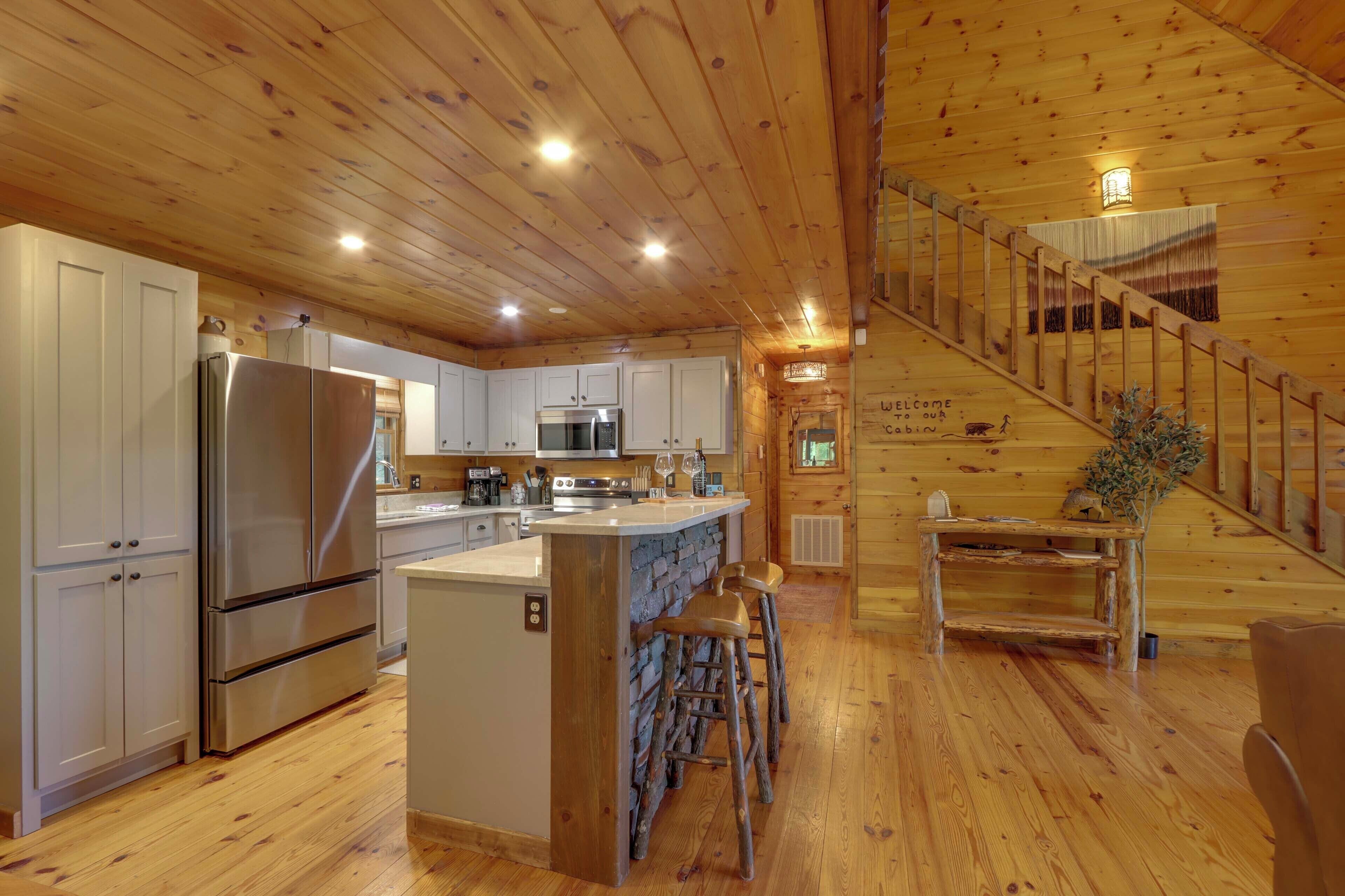 A wooden cabin interior with a kitchen, a dining area, and a staircase.