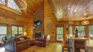 A cozy cabin interior with a stone fireplace, wooden floors, leather sofas, and a bar area. - Family Friendly: Hot Tub Haven in Mineral Bluff! (Mineral Bluff)