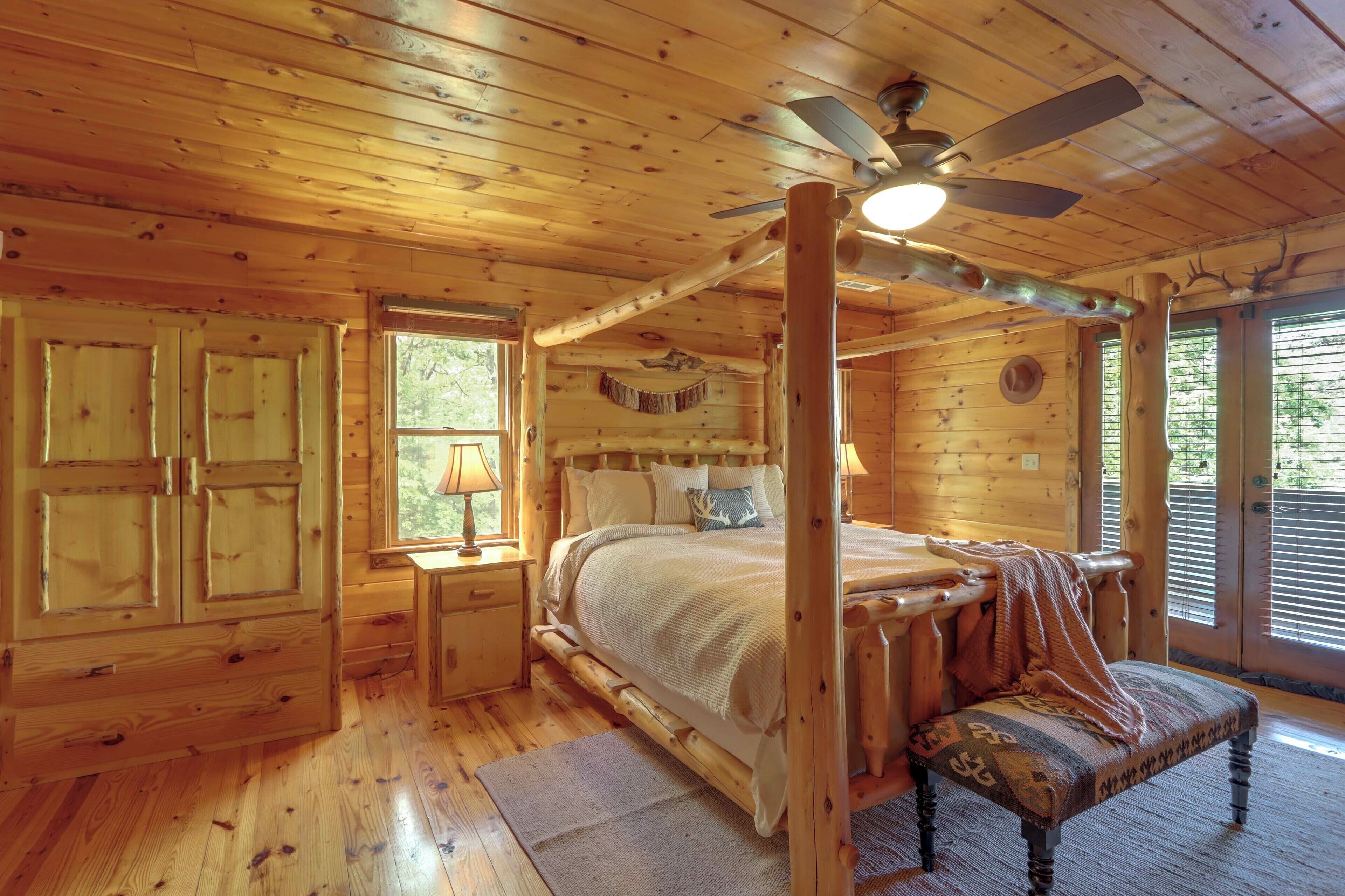 A log cabin bedroom with a four-poster bed, wooden walls, and a ceiling fan.