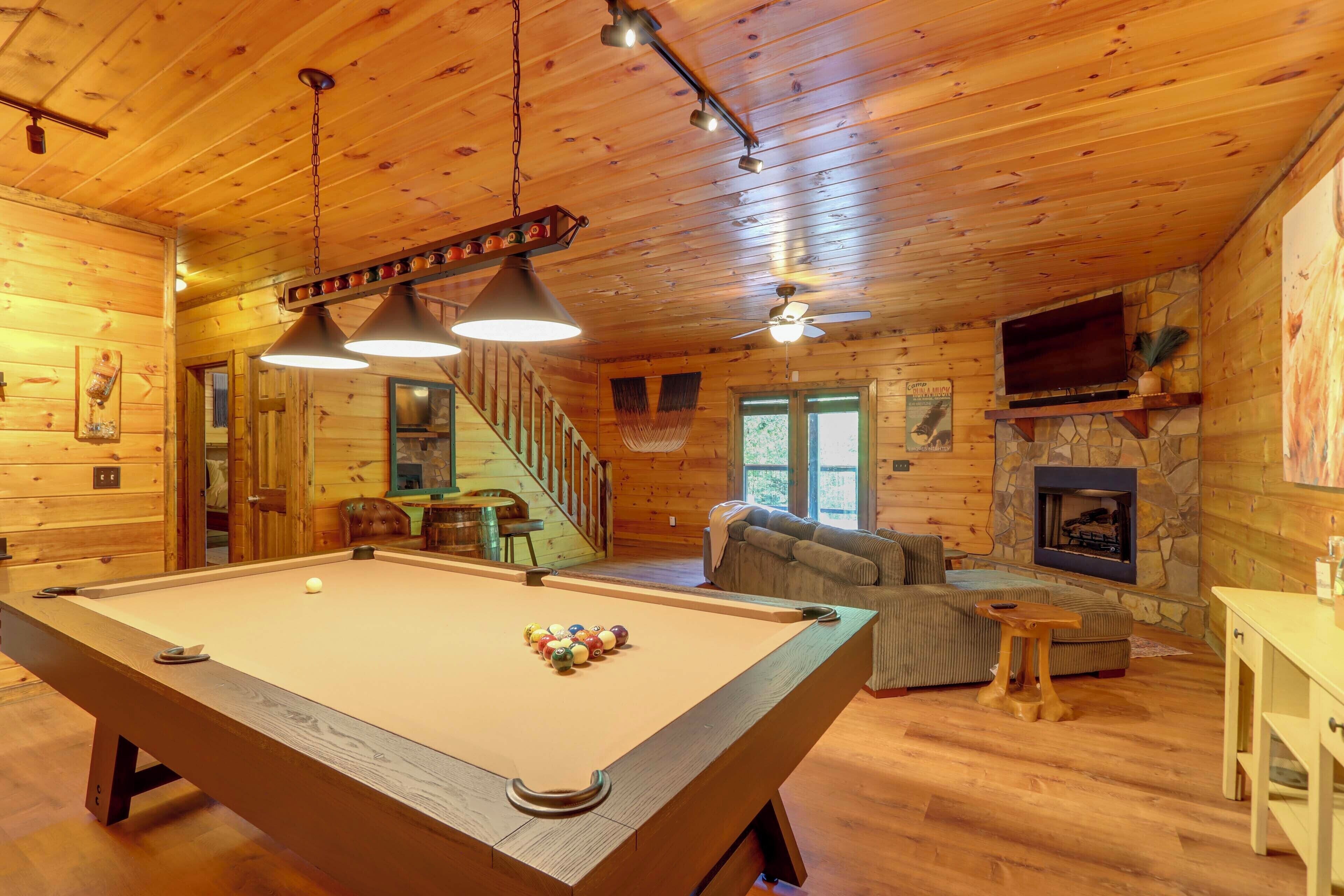 A wooden cabin interior with a pool table, a fireplace, a sofa, and a staircase.