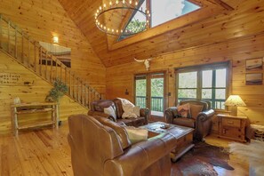 Interior de una cabaña con paredes de madera, un sofá de cuero, una araña y una escalera.