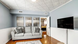 Un soggiorno con un divano grigio, un tappeto decorato e una televisione a schermo piatto su un mobile bianco.