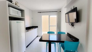 Une cuisine compacte avec un coin repas, un téléviseur fixé au mur et une fenêtre avec des rideaux.