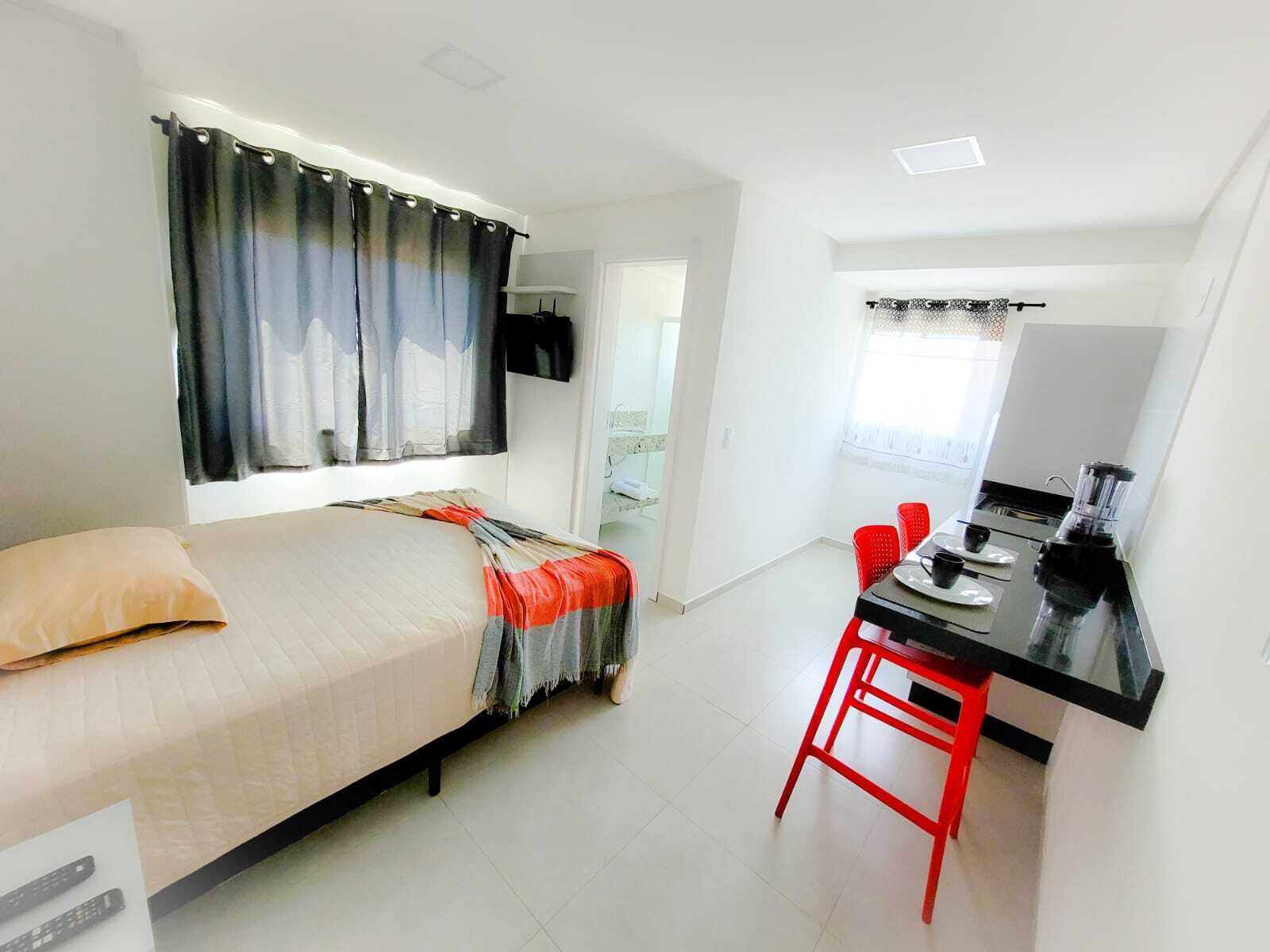 Un dormitorio con cama, escritorio y silla. Hay una ventana con cortinas, una puerta y un televisor instalado en la pared.