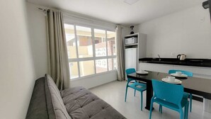 Un espace de vie compact comprenant un canapé, une table à manger avec des chaises, un coin cuisine et une grande fenêtre.