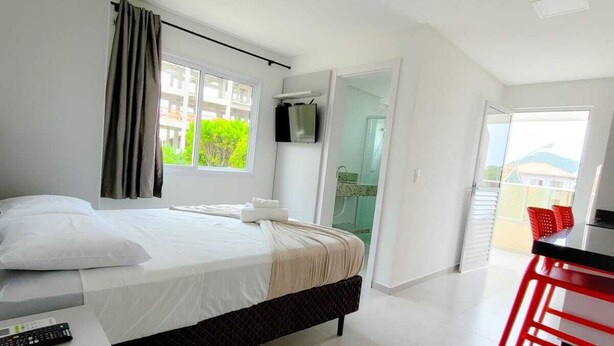 Une chambre d’hôtel moderne équipée d’un lit, d’une télévision, d’un bureau avec une chaise et d’un balcon avec des chaises rouges.