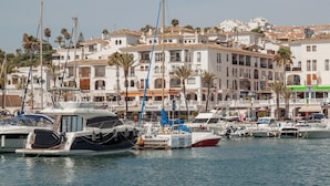 A marina with boats docked, surrounded by white buildings with balconies and palm trees. - Penthouse with sea and mountain views on the Costa del Sol. (Manilva)